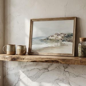 Puede incluir: Una estanter&iacute;a de madera exhibe una pintura enmarcada de un paisaje costero, dos tazas de cer&aacute;mica, un tarro de cristal con tapa de corcho y una jarrita. Los objetos son de tonos neutros.