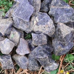 May include: A collection of rough, dark blue and gray stones with a natural, irregular shape. The stones are scattered on a bed of dry grass and leaves.