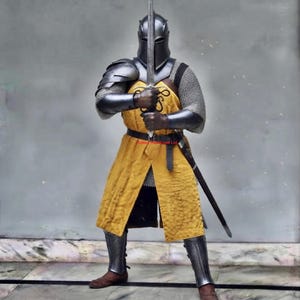 May include: A suit of armour featuring a dark metal helmet, shoulder pauldrons, arm guards, and greaves over a chainmail shirt. A long, mustard-yellow surcoat is worn over the armour, secured by a black leather belt with a sword scabbard.