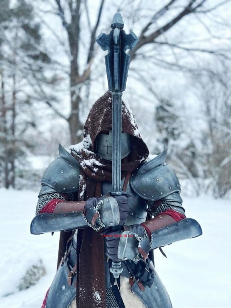 May include: A person in medieval armor holding a spiked mace. The armor is a weathered gray with red accents and chainmail. The person is wearing a brown hood and is standing in a snowy environment.
