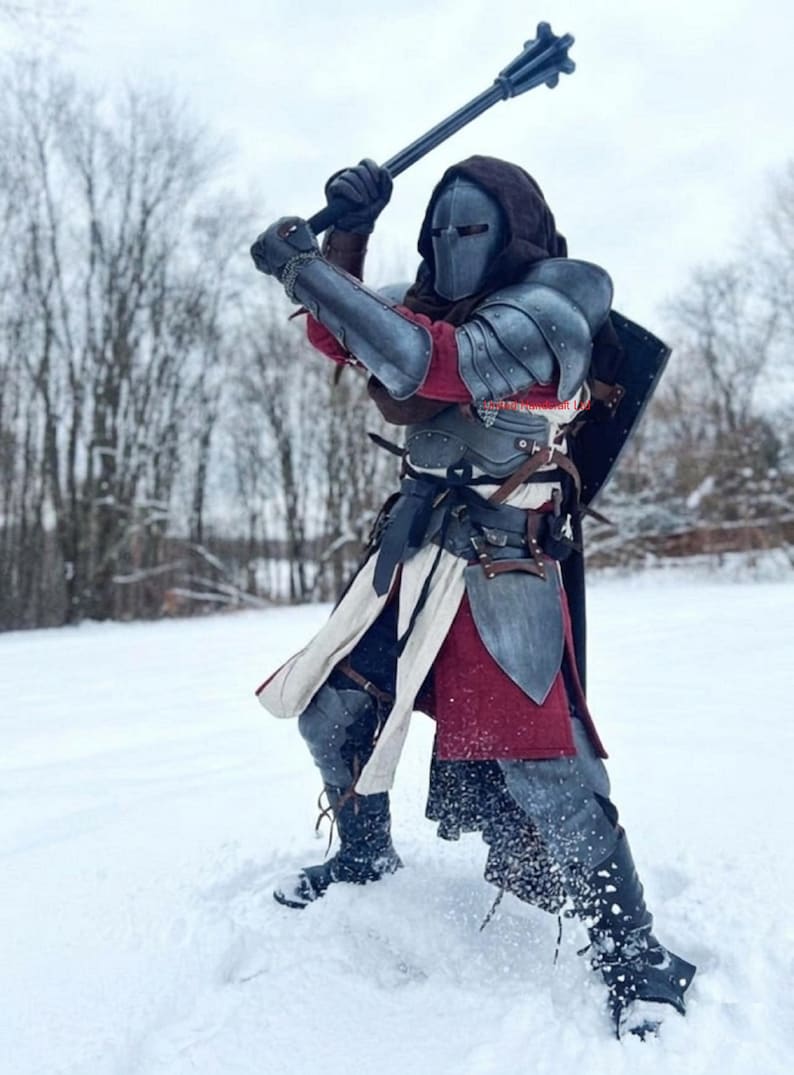 May include: A person in medieval-style armor, wielding a spiked mace in a snowy environment. The armor is a mix of silver and gray, with red and white accents. The person is wearing a helmet and a hooded cloak.