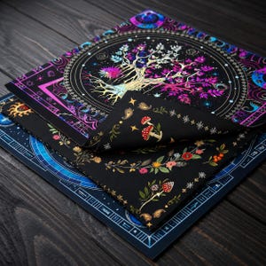May include: Two square fabric cloths with black backgrounds. The top cloth features a central tree with pink and blue leaves surrounded by circular patterns. The folded corner reveals a black fabric with colourful mushroom and floral botanical prints.