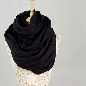 May include: A black infinity scarf made of soft fabric. The scarf is draped around a mannequin's neck and is styled in a loose, flowing way.