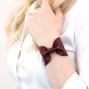 May include: A brown leather bracelet with a bow detail.
