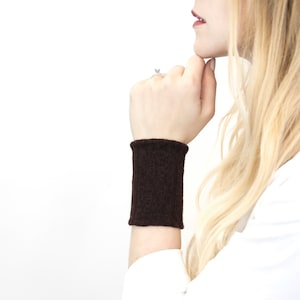 May include: A brown knitted wrist warmer. The warmer is ribbed and has a simple design.