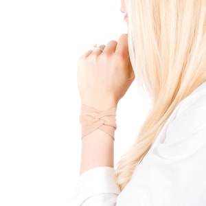 May include: A close-up of a woman's wrist wearing a light brown braided fabric bracelet.