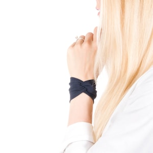 May include: A close-up of a woman's wrist wearing a dark blue fabric wristband with a knotted design.