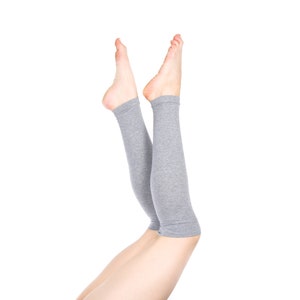 May include: A pair of gray leg warmers with ribbed texture. The leg warmers are worn on a person's legs, with the feet pointing upwards.