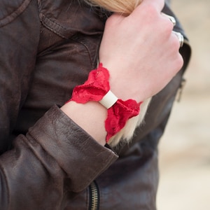 May include: A red lace bracelet with a white metal buckle. The bracelet is worn on a person's wrist.