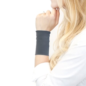 May include: A gray arm warmer made of soft fabric. The arm warmer is worn on the left wrist of a person.