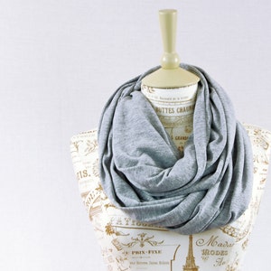 May include: A gray infinity scarf made of soft fabric. The scarf is draped around a mannequin's neck and is displayed against a white background.