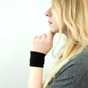 May include: A woman wearing a black wrist cuff. The cuff is made of a soft, stretchy material and has a simple, minimalist design.