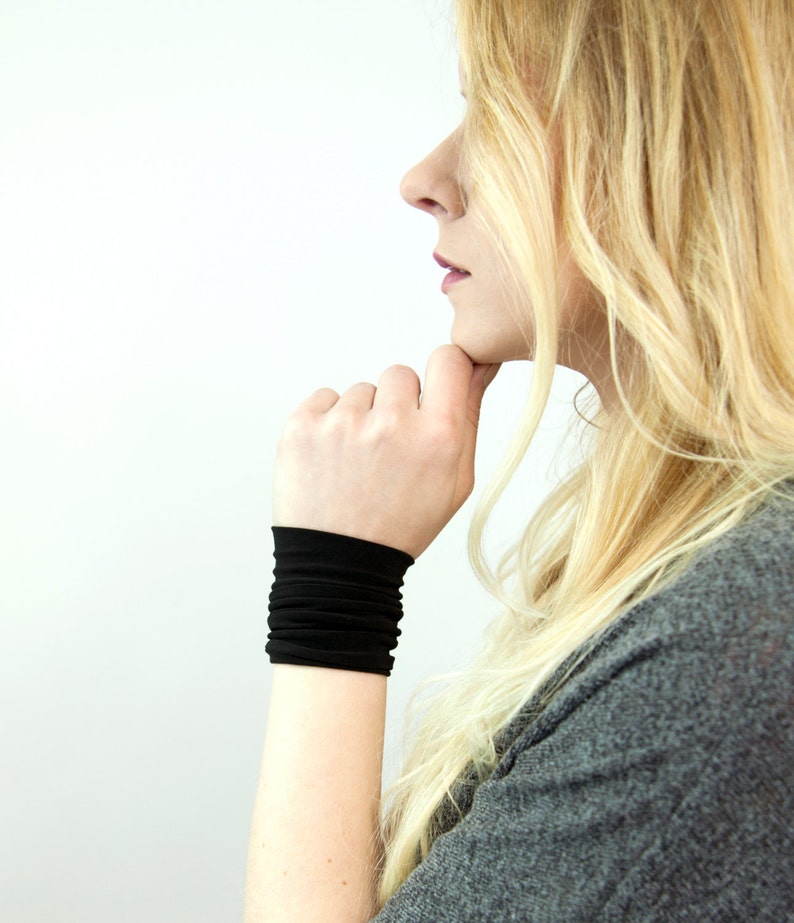 May include: A woman wearing a black wrist cuff. The cuff is made of a soft, stretchy material and has a simple, minimalist design.