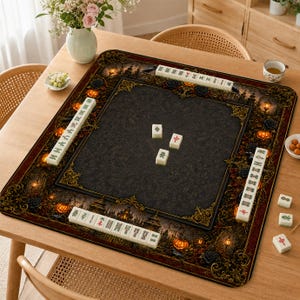May include: A square mahjong mat featuring a dark, gothic-inspired border with orange pumpkins, black roses, and ornate gold filigree. The center is a solid dark gray with a subtle damask pattern, holding three white mahjong tiles with red and green symbols.