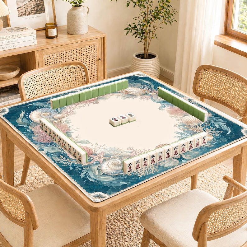 May include: A wooden square Mahjong table with a marine-themed mat featuring seashells and coral. The table is surrounded by rattan chairs and is set with green and white tiles. The table is approximately 36 inches square.