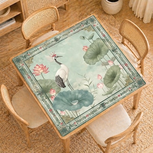 May include: Square wooden table with a painted top featuring a crane, lotus flowers, and lily pads in shades of green, pink, and white. The table is surrounded by four wooden chairs with woven backs, set on a woven rug.