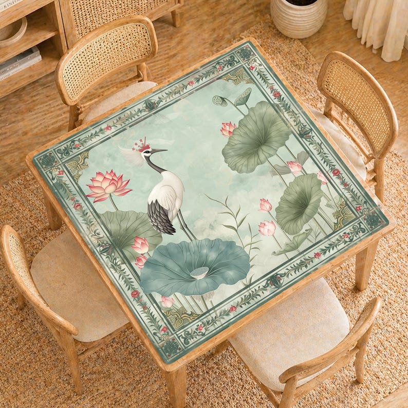 May include: Square wooden table with a painted top featuring a crane, lotus flowers, and lily pads in shades of green, pink, and white. The table is surrounded by four wooden chairs with woven backs, set on a woven rug.