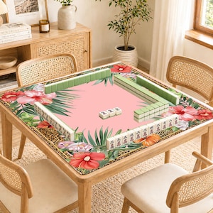 May include: A wooden mahjong table with a pink playing surface, edged with floral and leopard print borders. Green and white mahjong tiles are arranged on the table. The table is surrounded by four rattan chairs. The table is approximately 100 cm square.
