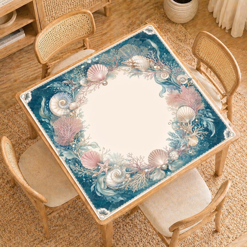 May include: Square wooden table with a marine-themed design. The table features a cream-colored center surrounded by a border of seashells, coral, and pearls in shades of pink, blue, and beige. The table is surrounded by four wooden chairs.