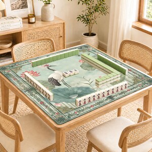 May include: A wooden square Mahjong table with a green and floral patterned mat. The mat features a crane, lotus flowers, and Chinese characters. Green and white Mahjong tiles are arranged on the table, surrounded by four rattan chairs.