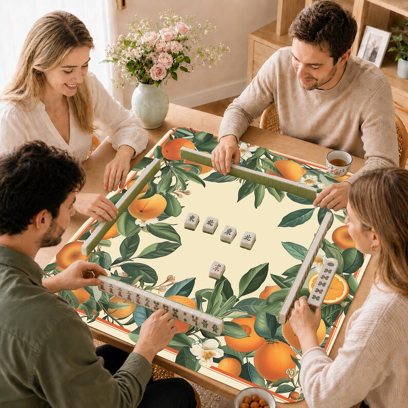 Może przedstawiać: Kwadratowa mata do mahjonga z kremowym tłem i żywym wzorem pomarańczowych owoc&oacute;w cytrusowych oraz zielonych liści. Na macie znajduje się kilka płytek do mahjonga ułożonych na środku i wzdłuż krawędzi, wraz z ilustracjami pomarańczy.