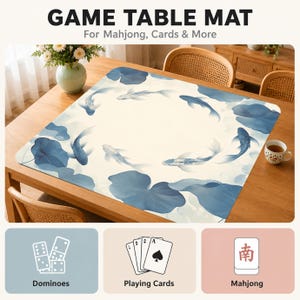 May include: A square game table mat featuring a cream-colored background with a pattern of blue koi fish and large blue lily pads. The text GAME TABLE MAT For Mahjong, Cards & More is at the top, with icons for dominoes, cards, and mahjong below.
