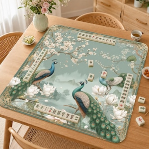 May include: A square mahjong mat featuring a light green background with illustrations of two peacocks, white lotus flowers, and cherry blossom branches. The mat is bordered by gold-toned decorative patterns and includes several mahjong tiles.