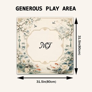 May include: A square play mat featuring a cream background with a decorative border, floral motifs, and koi fish. The center displays the letters MJ. Text at the top reads GENEROUS PLAY AREA. Arrows indicate dimensions of 31.5 inches by 31.5 inches.