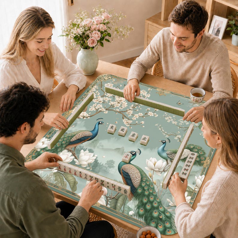May include: A square mahjong mat featuring a light green background with illustrations of two peacocks, white lotus flowers, and cherry blossom branches. The mat includes four mahjong tiles with the Chinese characters for north, east, south, and west.