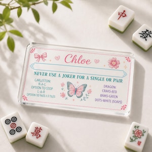 May include: A rectangular acrylic Mah Jongg card featuring the name Chloe, a pink butterfly, and floral accents. The text reads: NEVER USE A JOKER FOR A SINGLE OR PAIR, CARLESTON: R-A-L, OPTION TO STOP L-A-R, OPTION TO PASS 1-3 TILES, DRAGON: CRAKS-RED, BAMS-GREEN, DOTS-WHITE (SOAPS).