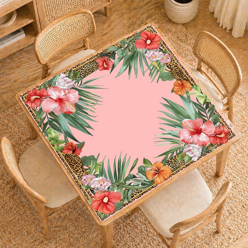 May include: A square table with a pink surface, decorated with a floral design of red hibiscus flowers, green leaves, and a leopard print border. The table is surrounded by four wooden chairs with woven backs.
