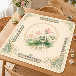 May include: A square mahjong mat with a cream-colored surface featuring a central circular border and a watercolor-style lotus flower illustration. The mat includes green decorative corner patterns and several mahjong tiles arranged in rows.