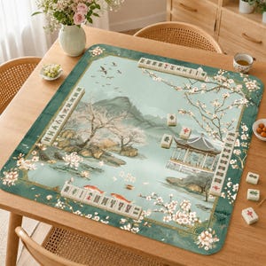 May include: A rectangular mahjong mat featuring a light green landscape illustration with cherry blossoms, a pavilion, and koi fish. The mat is decorated with rows of ivory-colored mahjong tiles arranged along the edges and center, displaying various traditional symbols and characters in red, green, and black ink.