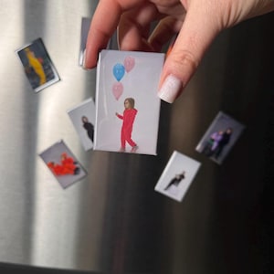 May include: A rectangular magnet featuring a child in a red jumpsuit holding blue and pink balloons. Several other magnets with various images are also visible.