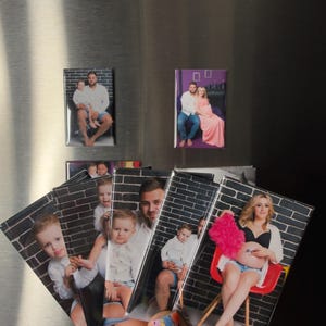 May include: A collection of rectangular photo magnets featuring family portraits. The magnets are displayed on a refrigerator door. The photos depict a family with a child and a pregnant woman.