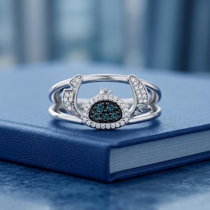 May include: A silver ring featuring a character design with a blue and white gemstone center. The ring has a unique, open design with small white gemstones and a detailed character face.
