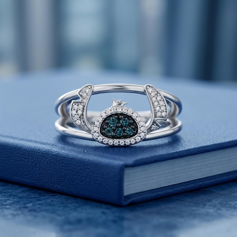 May include: A silver ring featuring a character design with a blue and white gemstone center. The ring has a unique, open design with small white gemstones and a detailed character face.