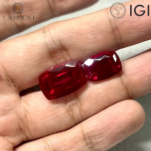 May include: Two loose, cushion-cut rubies with a deep, vibrant red color and faceted surfaces. The gemstones are displayed against a neutral background, with the Tahani logo and IGI certification text visible in the upper corners of the frame.