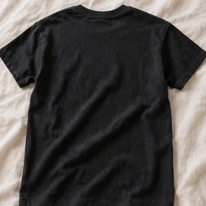 May include: A solid black short-sleeved t-shirt featuring a classic crew neckline. The garment is displayed flat, showcasing the plain back side of the shirt with visible stitching along the sleeves, hemline, and collar, maintaining a simple design.