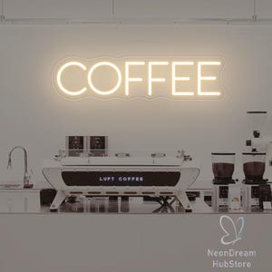 May include: A neon sign displaying the word "COFFEE" in a white, rounded font. Below, a white and black espresso machine with the text "LUFT COFFEE" is visible. The image suggests a coffee shop or cafe setting.