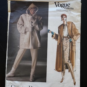 May include: A vintage Vogue Patterns sewing pattern featuring a Christian Dior design. The pattern envelope displays illustrations of a hooded coat and a long coat with matching pants. The text "Vogue Patterns Paris Original" is visible.