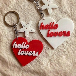 Può includere: Due portachiavi con ciondoli a forma di cuore con la scritta "hello lovers". Un cuore è rosso, l'altro bianco. Ogni portachiavi ha un ciondolo a forma di stella marina bianca e un anello color argento.