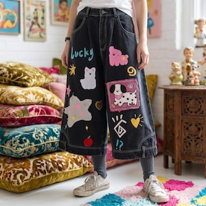 Può includere: Culotte in denim nero con toppe colorate e la scritta "lucky" in turchese. Le toppe includono un orsetto rosa, un gatto bianco, un cane dalmata, stelle e cuori. I pantaloni sono indossati con scarpe da ginnastica bianche.