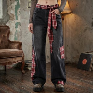 Può includere: Pantaloni larghi in denim nero con dettagli a quadri rossi e bianchi. I pantaloni presentano toppe a quadri sui lati e una cintura abbinata annodata in vita. I pantaloni hanno un aspetto invecchiato.