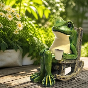以下が含まれることがあります： クリーム色の腹部を持つ緑色のカエルの置物が、茶色の質感のあるロッキングチェアに座っています。カエルは小さな白いカップを手に持っています。置物は暗い目と詳細な水かきのある足をしており、木製の表面に置かれています。