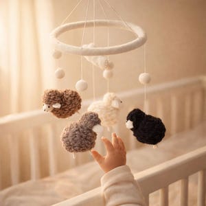 Puede incluir: Móvil para bebé con cinco ovejas de lana en tonos marrón, gris, blanco y negro. Las ovejas cuelgan de un anillo blanco con pompones blancos. Ideal para una cuna o habitación infantil.