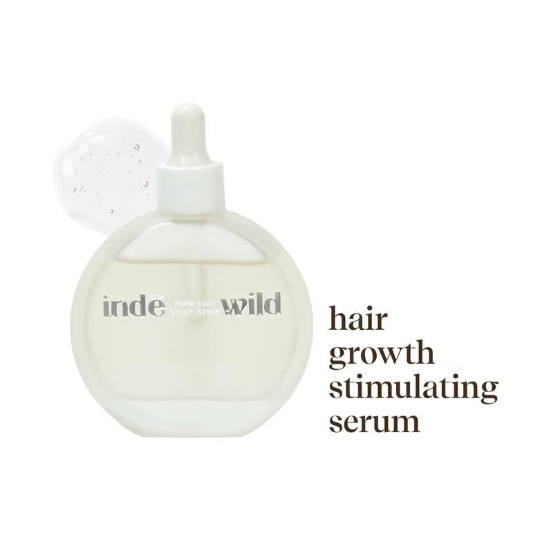 Op de afbeelding: Een heldere, ronde fles haargroei stimulerend serum met een witte druppelaar. Op de fles staat "inde wild". Een kleine hoeveelheid serum is zichtbaar naast de fles.