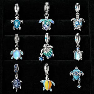 May include: A collection of nine silver-toned turtle charms with various designs. The charms feature blue, green, and yellow enamel details, some with sparkling accents. Each charm has a loop for attaching to a bracelet or necklace.