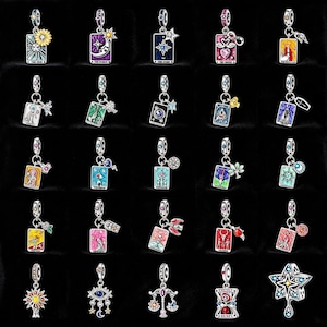 May include: A collection of silver-toned charm pendants featuring colorful tarot card designs. Each charm has a different design, including stars, moons, and flowers. The charms are suspended from a silver loop, suitable for bracelets or necklaces.