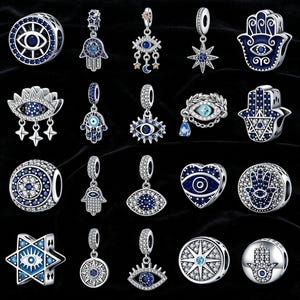 Puede incluir: Una colección de abalorios de plata con detalles de cristal azul y transparente. Los abalorios presentan varios diseños, incluyendo el ojo turco, la mano de Fátima y estrellas. Los abalorios se muestran sobre un fondo negro.
